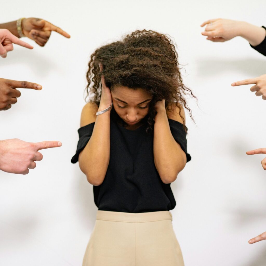 Женщина, ошеломленная, окруженная указывающими пальцами, изображающая издевательства.